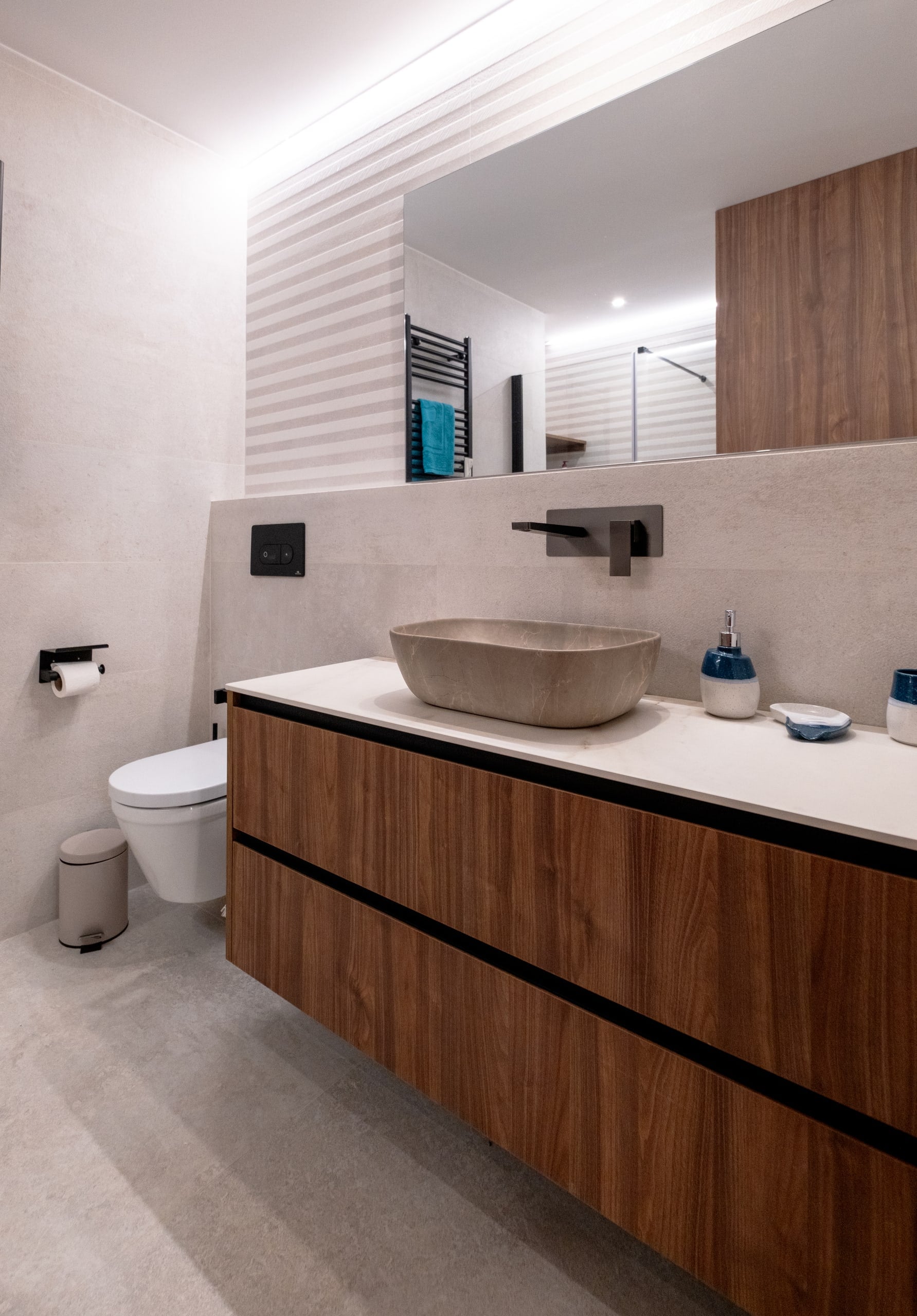 Baño con lavabo de piedra sobre encimera y mueble de nogal suspendido